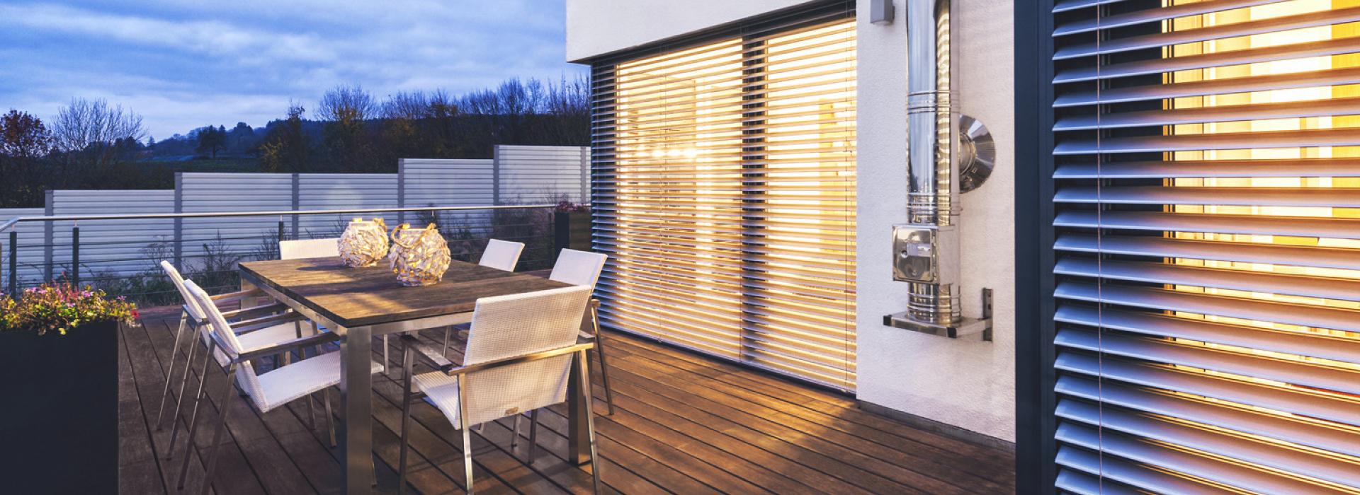 Terrasse mit Tischgruppe bei Dämmerung mit Blick auf Raffstoren