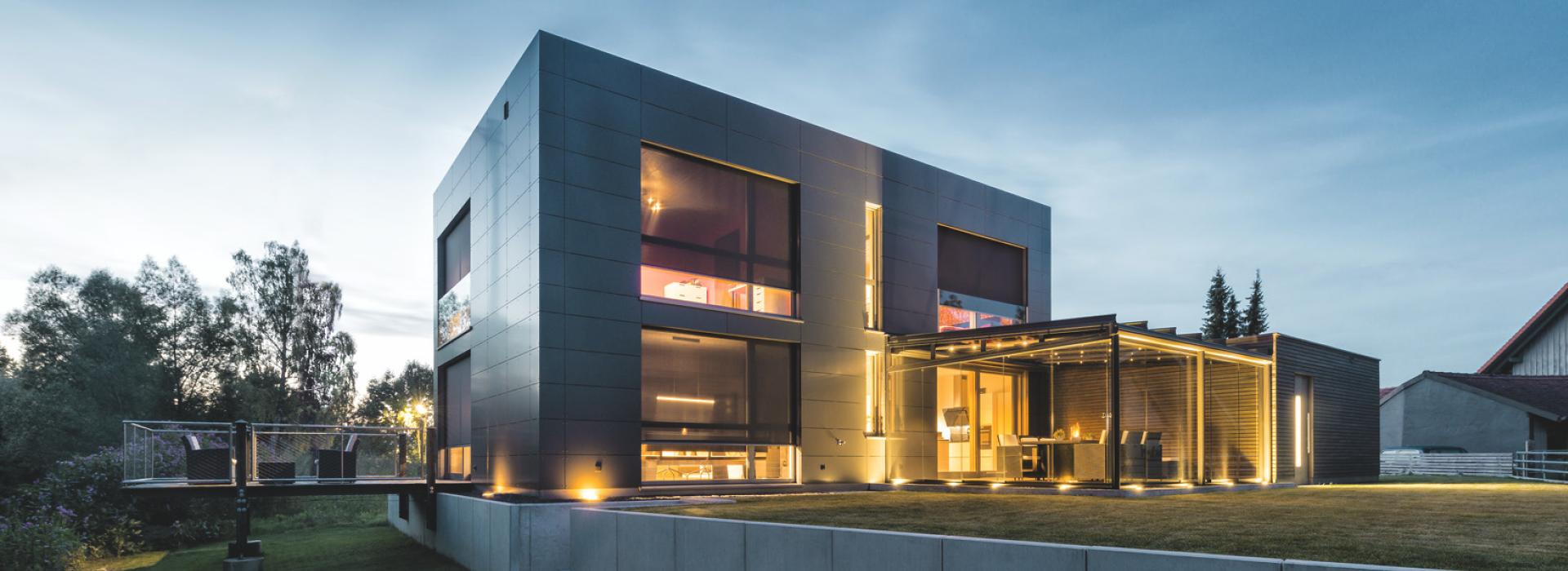 Modernes Haus bei Dämmerung mit Innenbeleuchtung und runtergelassenen Vorbautextilscreens