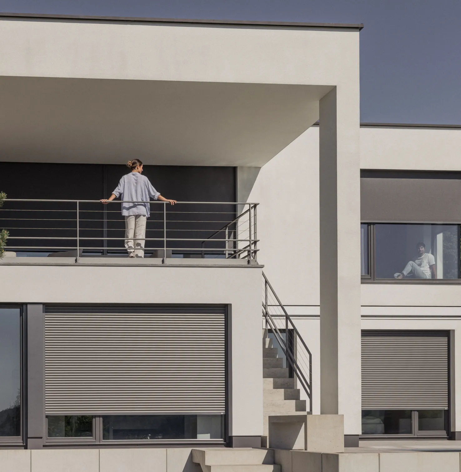 Haus mit Rollladen und Textilscreen mit einer Frau auf dem Balkon
